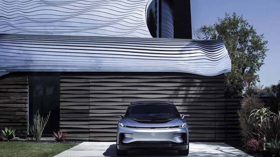 A silver Faraday FF 91 parked in front of a garage.