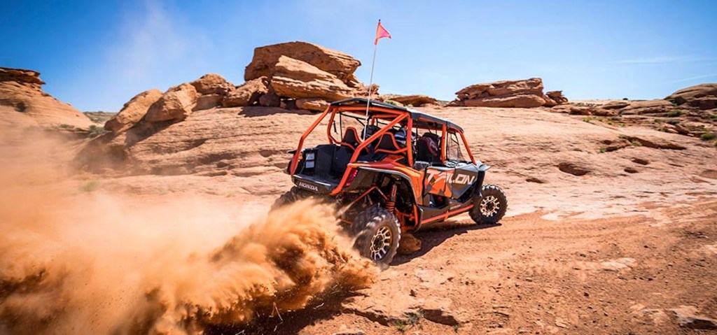 An orange Honda Talon side-by-side UTV model driving fast on a sandy off-road trail