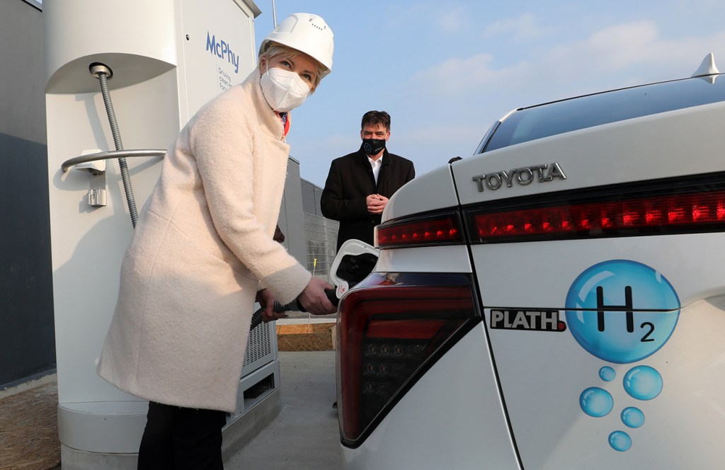 A woman refueling a hydrogen fuel cell vehicle at a hydrogen station.
