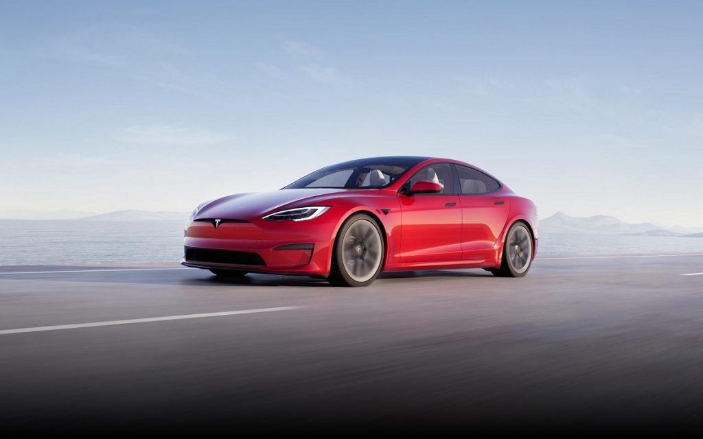 A red 2021 Tesla Model S driving with mountains in the background.