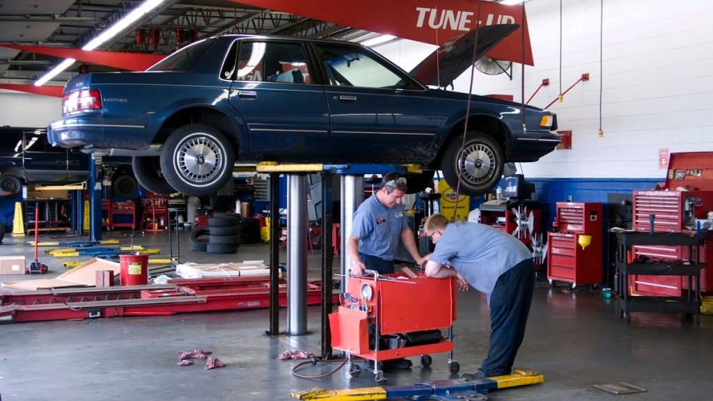 Maintenance being done to a blue car up on a lift in a garage.