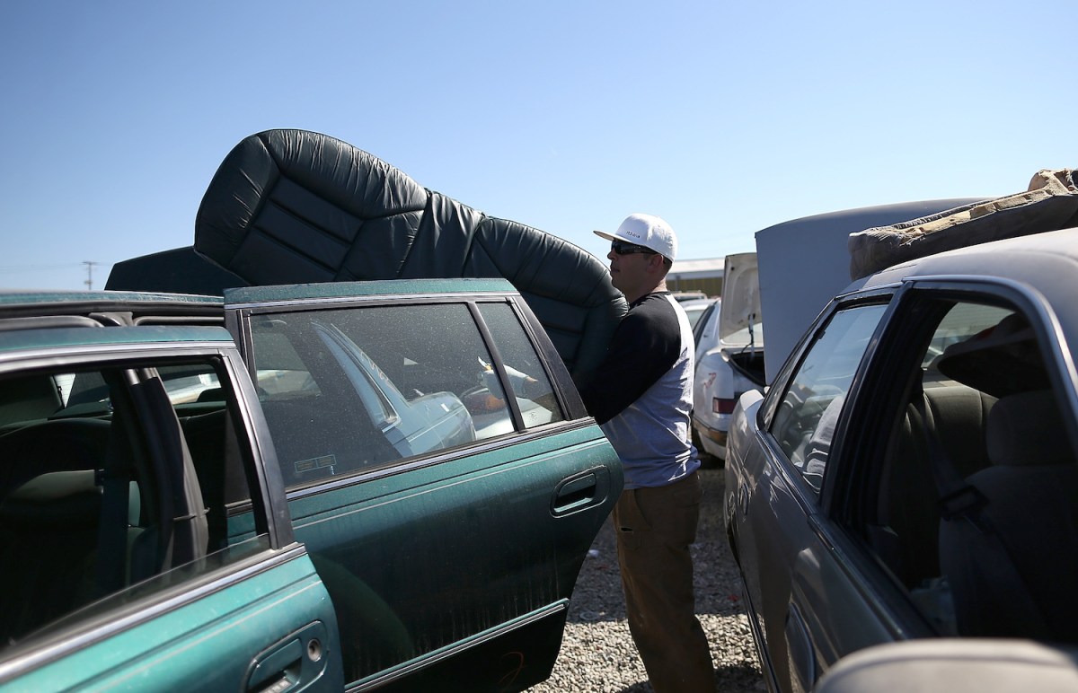 man removes a seat from a car at a salvage yard in Oakland ca