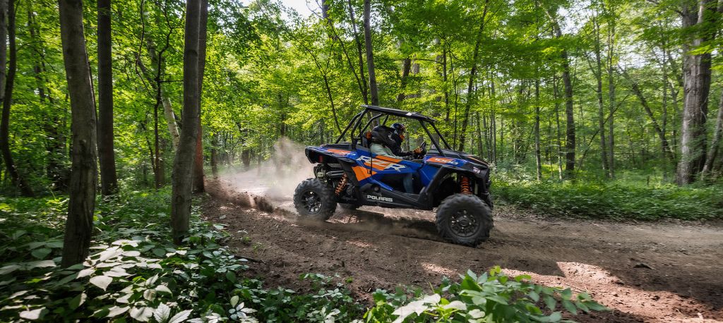 a blue and orange Polaris RZR XP 1000 driving off-road in the forest