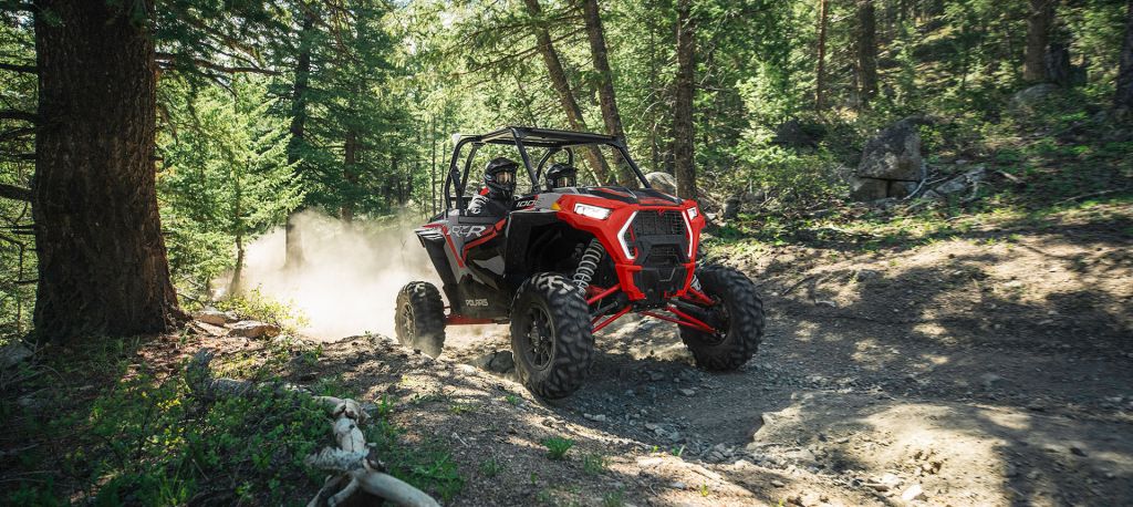a red Polaris RZR UTV driving off-road in the forest 