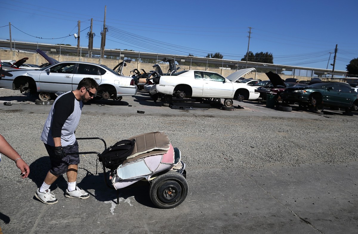 a man pushes a cart through a slavage yard in oakland, ca