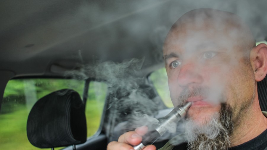 A bearded man vapes while driving a car