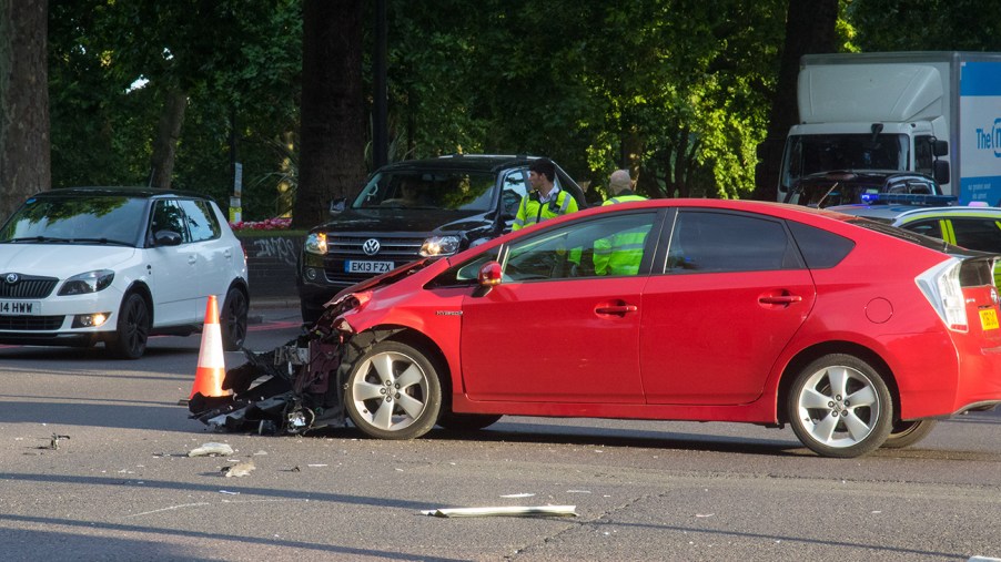 A badly damaged red Toyota Prius in the middle of the road after an accident.