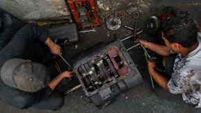 Colombian car mechanics work on a transmission in a car