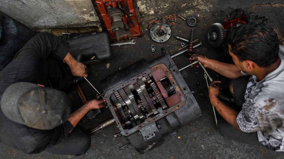 Colombian car mechanics work on a transmission in a car