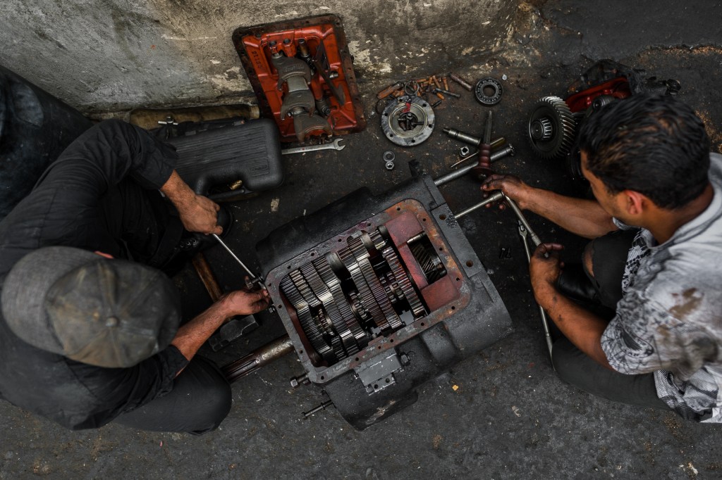 Colombian car mechanics work on a transmission in a car