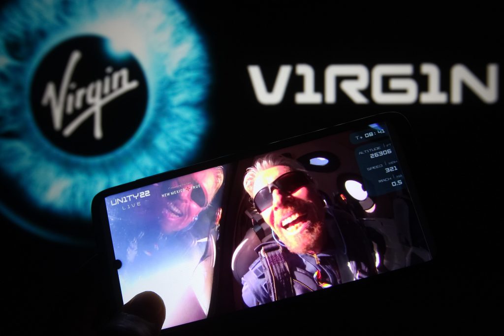  In this photo illustration, British billionaire Richard Branson is seen on a fragment of a Virgin Galactic Unity 22 Spaceflight Livestream Youtube video displayed on a smartphone with the Virgin Galactic logo in the background. 