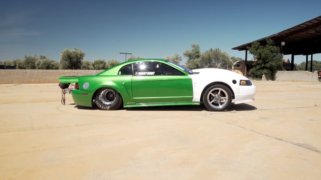 Nicky Bobby's  2000 Ford Mustang drag race car. The body of the car is mostly metallic green but the front end is in an unpainted white primer color. The car has an odd stance in which the rear sits much lower than the front.