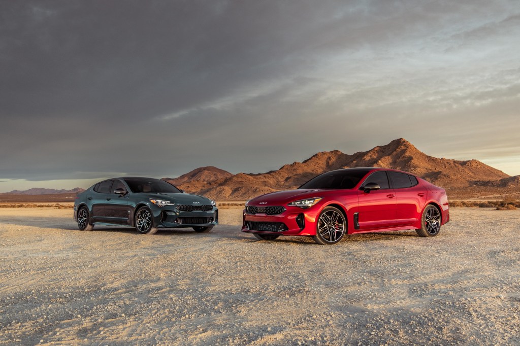 A red 2022 Kia Stinger GT and a Stinger GT-line photographed on in the desert together from the front 3/4 angle