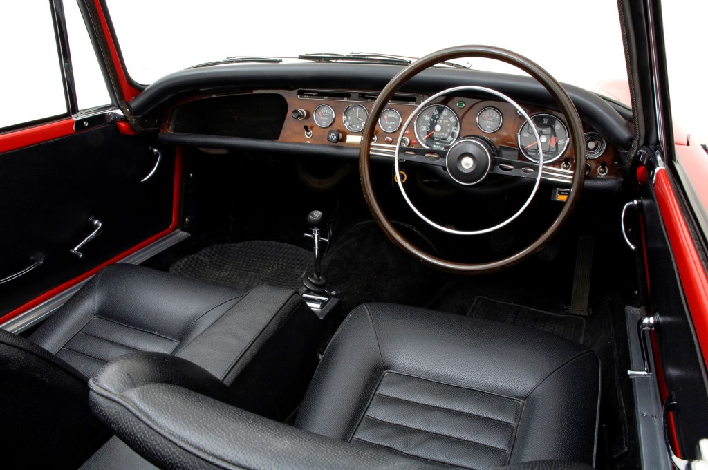 The black-leather-upholstered seats and wood-trimmed dashboard of a red British-market 1965 Sunbeam Tiger MKI