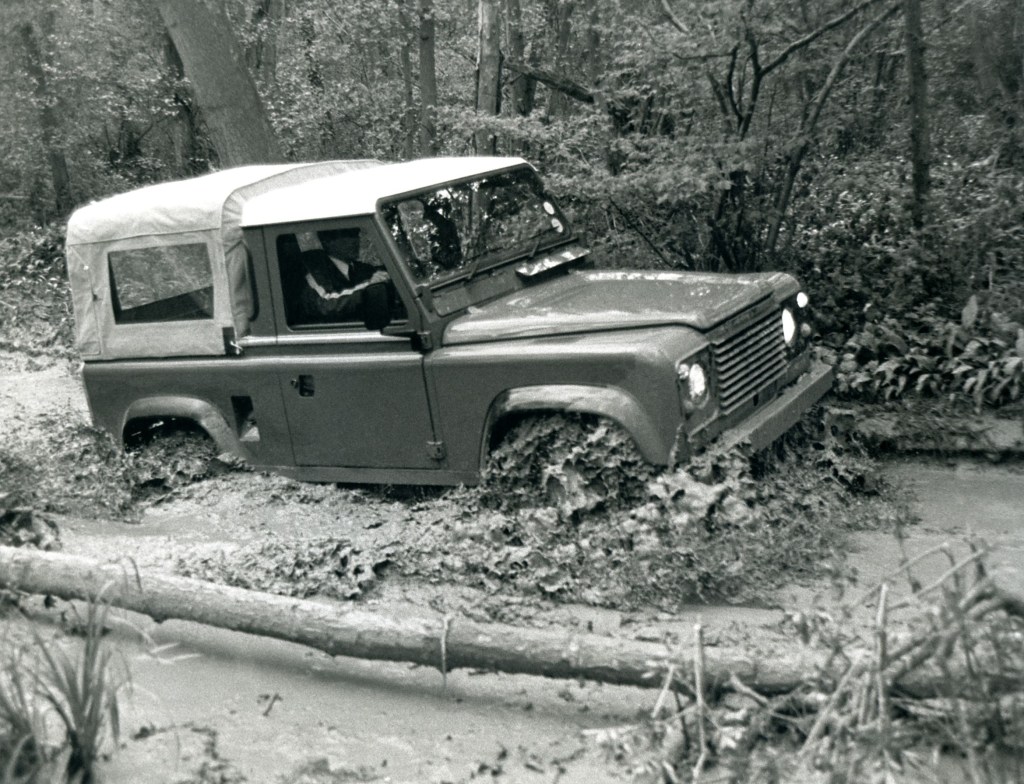 A 1984 Land Rover 'Defender' 90 off-roading through a muddy forest river