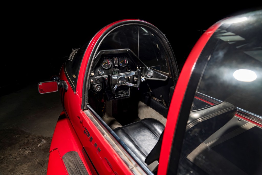 The dashboard and front seat of a red 1985 Pulse Litestar Autocycle with its canopy open