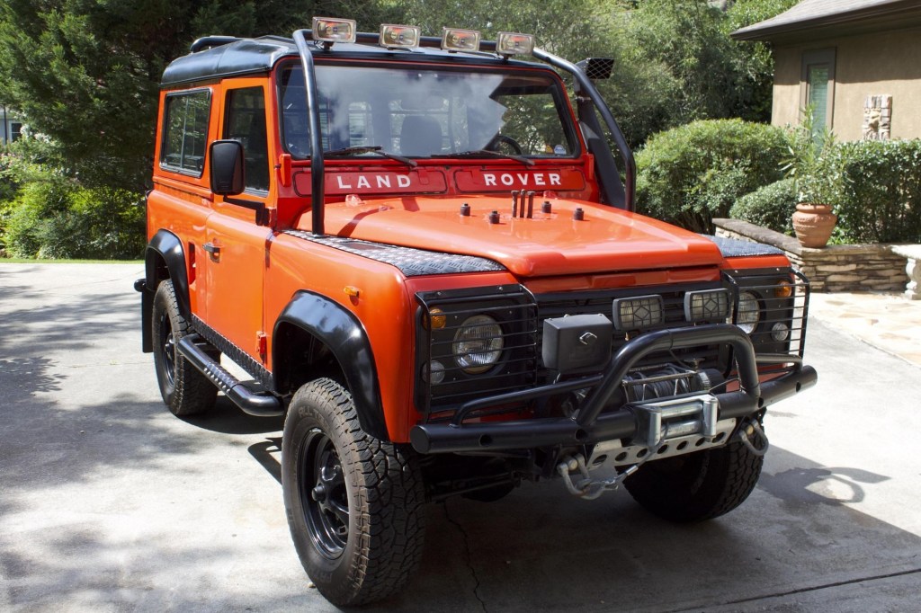 The front 3/4 view of a red modified red 1987 Land Rover 'Defender' 90 in a driveway