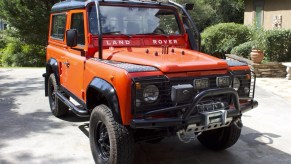 The front 3/4 view of a red modified red 1987 Land Rover 'Defender' 90 in a driveway