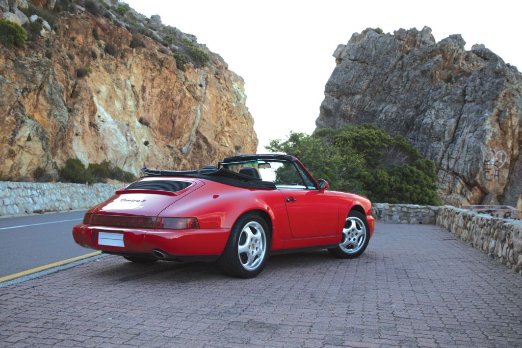 The rear 3/4 view of a red 1990 964 Porsche 911 Carrera 2 Cabriolet on a South African mountain road