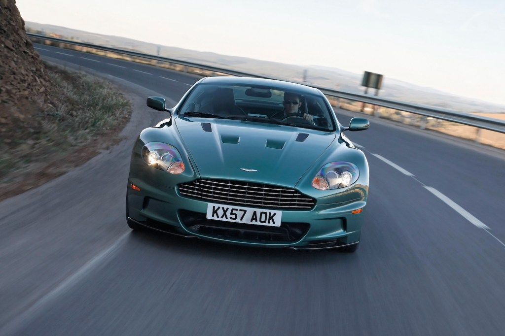 This is a publicity photo of a green Aston Martin DBS V12 grand tourer driving down the highway. This is one car both James Bond and Jay Leno own.