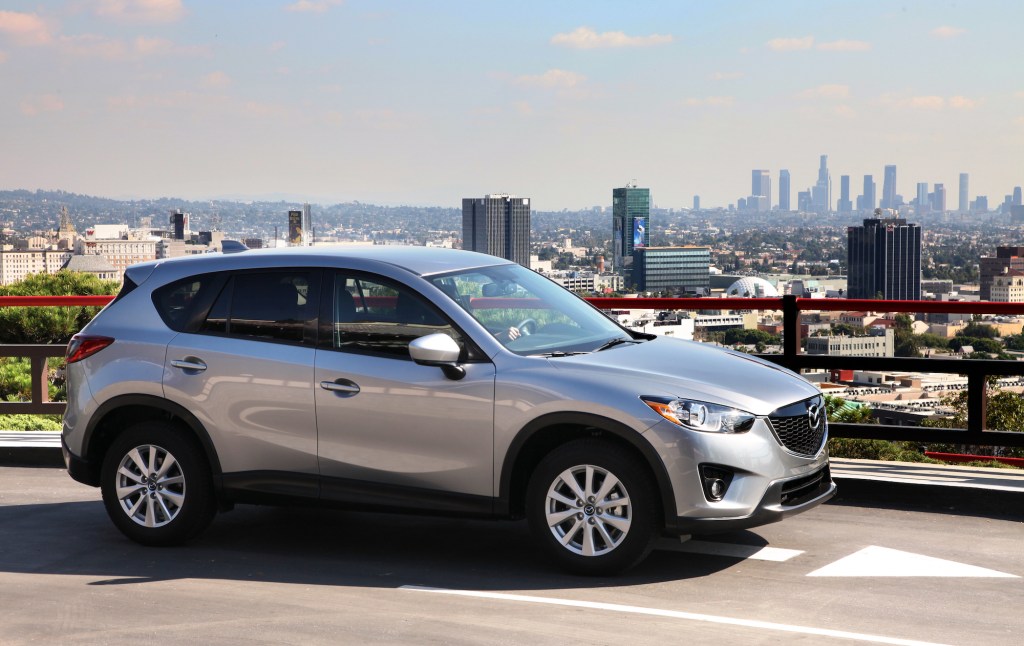 A silver 2014 Mazda CX-5 parked on a road overlooking a city skyline