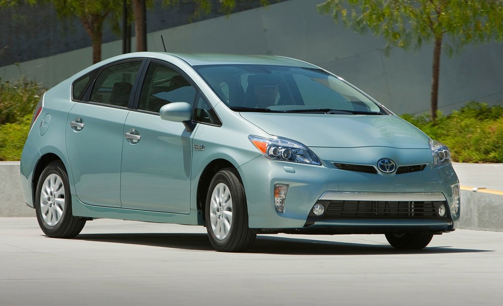 A green 2014 Toyota Prius Plug-In Hybrid drives on a road
