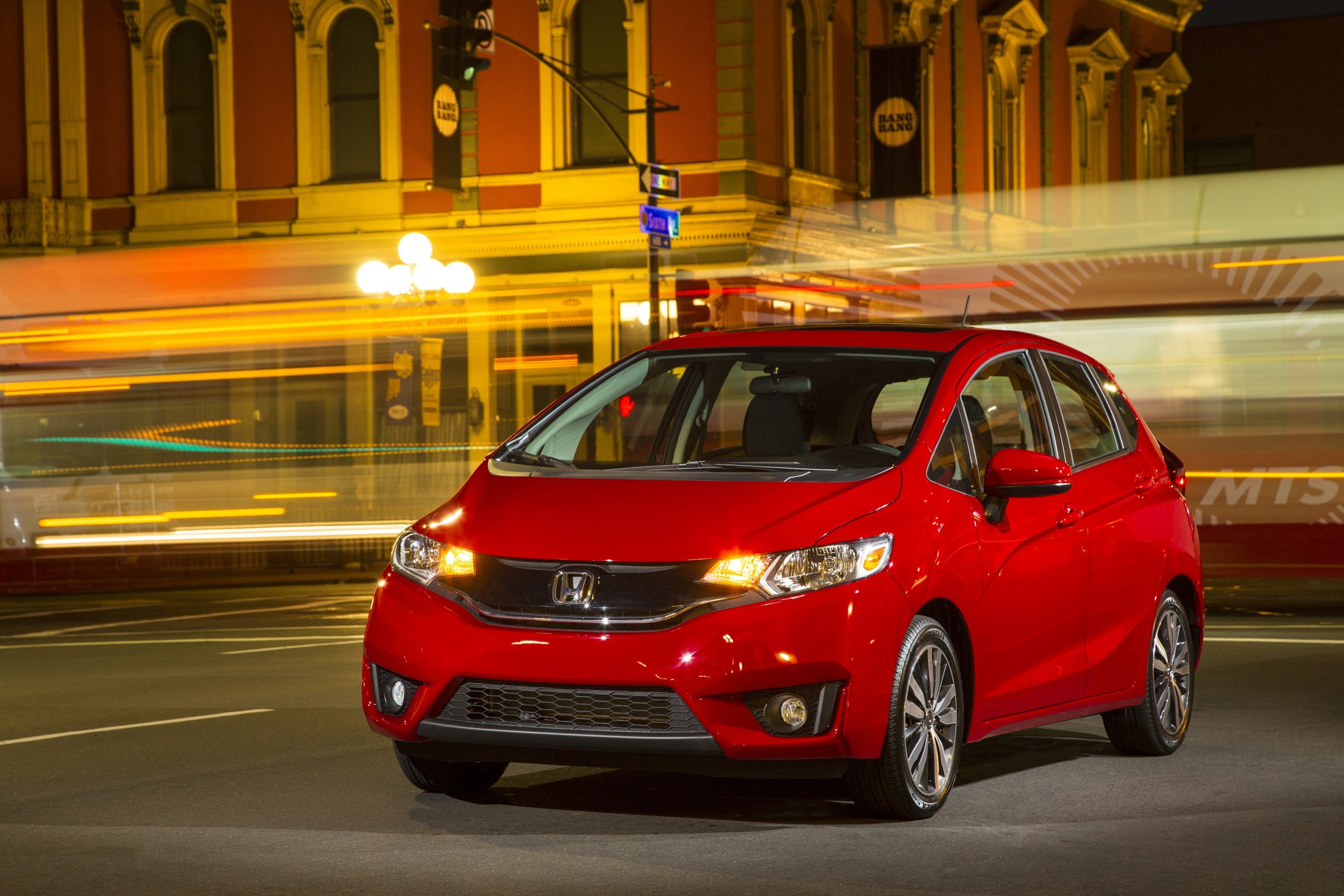 A red 2015 Honda Fit shot on a long exposure setting at night, making the traffic behind blur