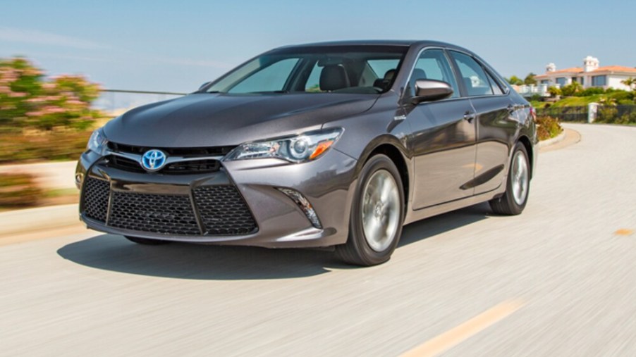 A grey 2015 Toyota Camry Hybrid driving on a sunny day
