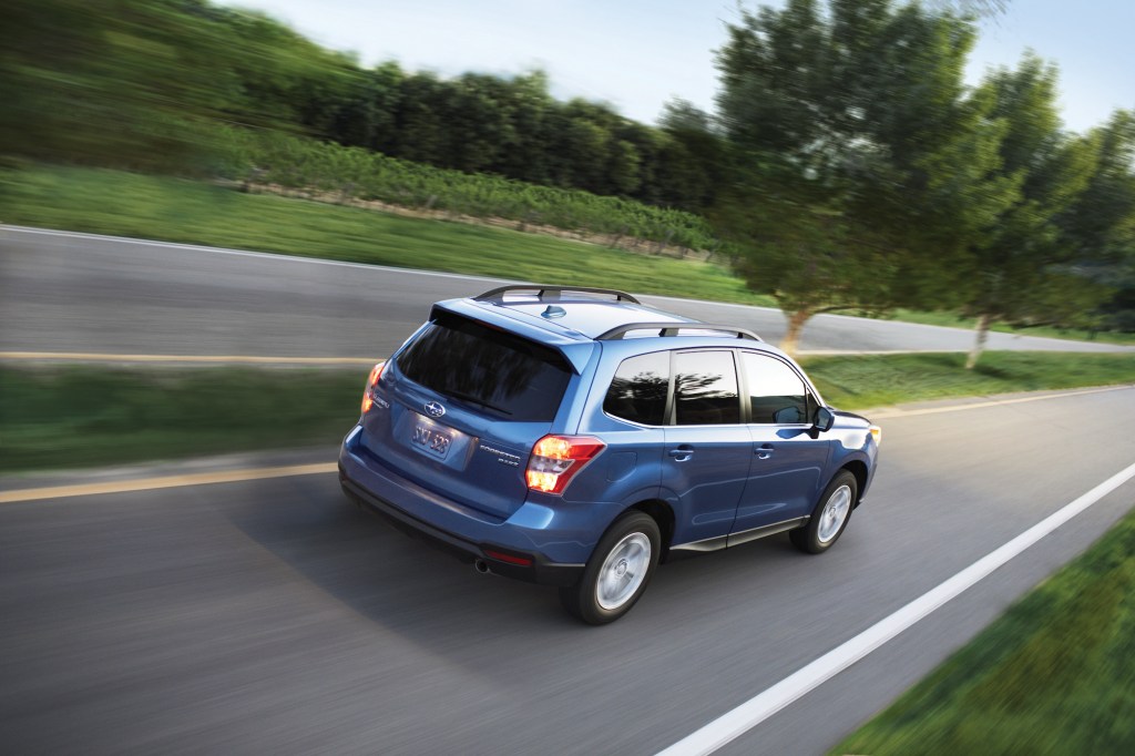A blue metallic 2016 Subaru Forester 2.5i travels on a road with a grassy medium dotted with trees