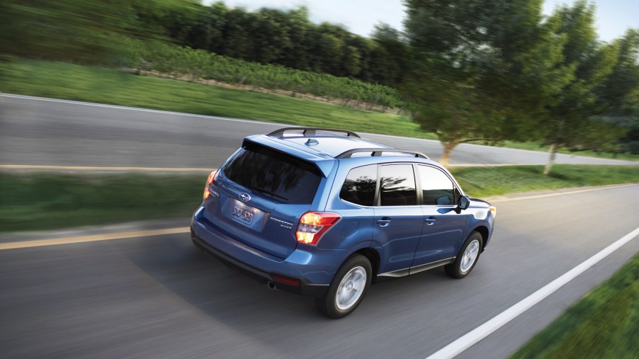 A blue metallic 2016 Subaru Forester 2.5i travels on a road with a grassy medium dotted with trees