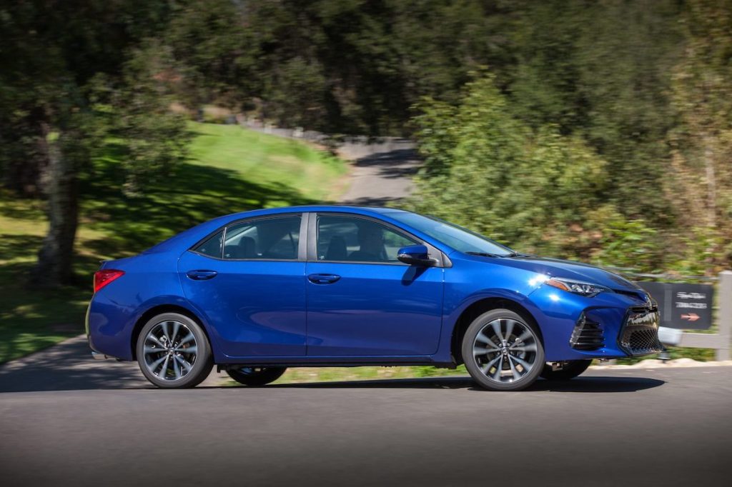A blue 2017 Toyota Corolla SE traveling on a country road surrounded by green hills and trees