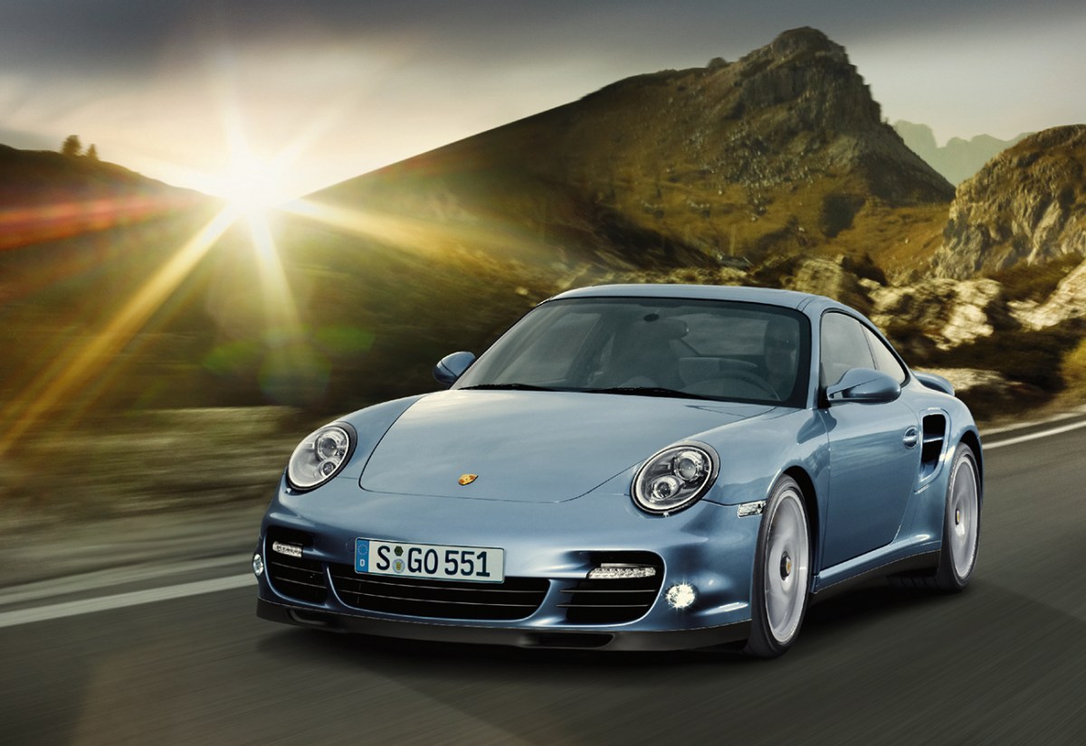 2018 Porsche 911 Turbo S seen in light metallic blue driving on a road at sunset. This car is similar to the 911 Turbo S seen in the drag race video featured in this article.