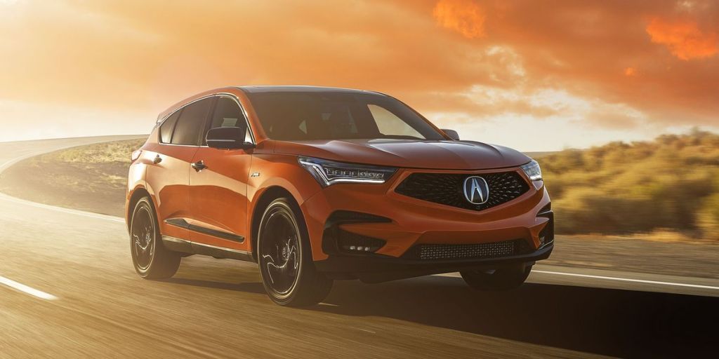 An orange 2021 Acura RDX driving down the road during a sunset