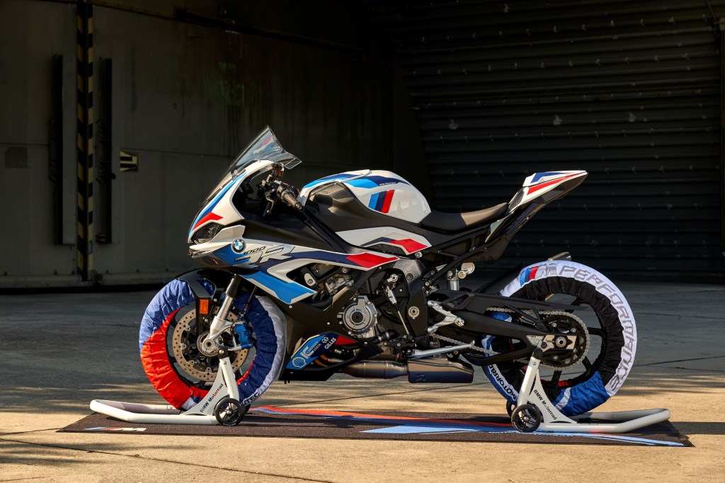 The side view of a white-blue-and-red 2021 BMW M 1000 RR on wheel stands with matching tire warmers