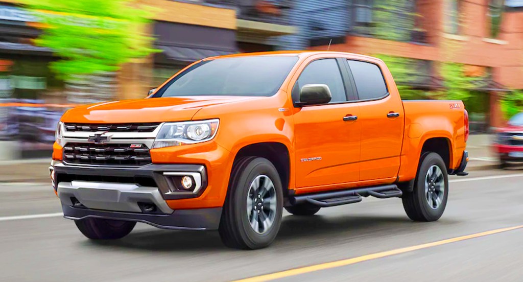 An orange 2021 Chevrolet Colorado pickup truck is driving on the road. 