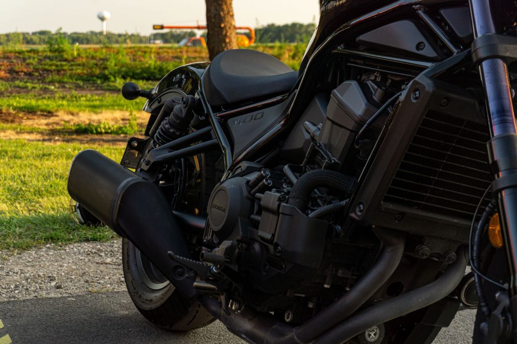 A closeup view of a black 2021 Honda Rebel 1100 DCT's engine, exhaust, seat, and rear suspension
