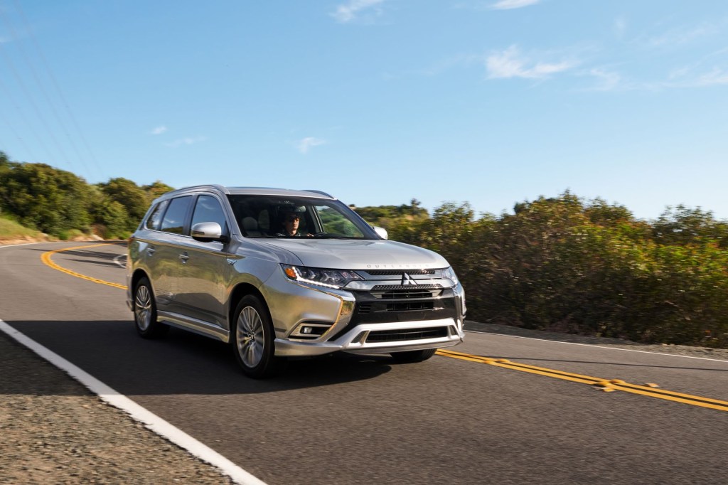 A 2021 Mitsubishi Outlander PHEV model in silver gray driving down a strip of highway