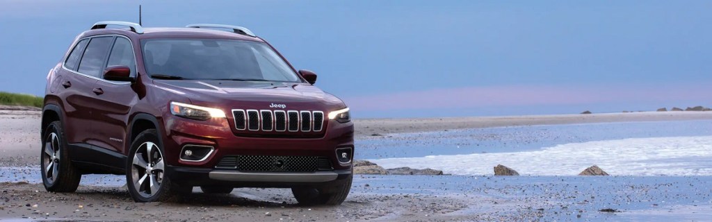 A red 2021 Jeep Grand Cherokee driving at the edge of the ocean. 