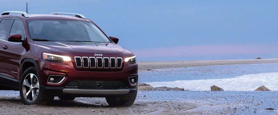 A red 2021 Jeep Grand Cherokee driving at the edge of the ocean.