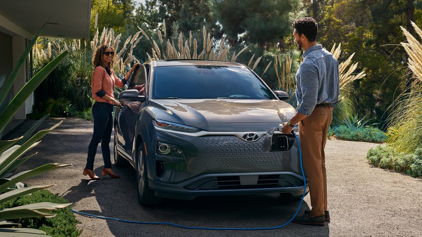 A taupe 2021 Hyundai Kona Electric being recharged by a couple.