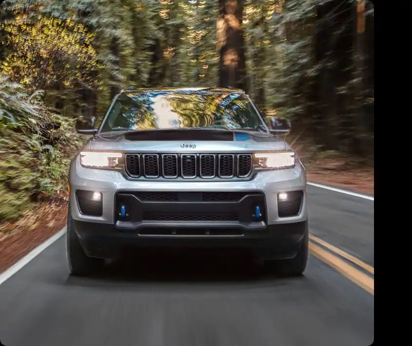 A silver 2022 Jeep Grand Cherokee driving down a wooded road.