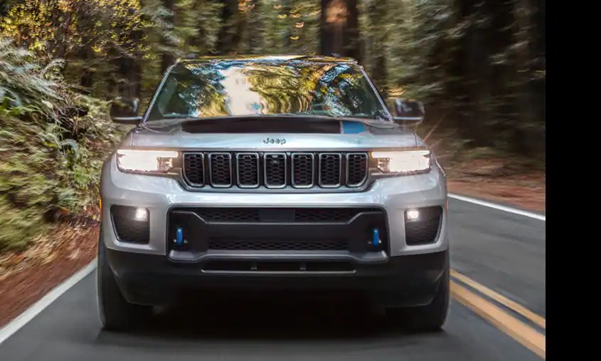 A silver 2022 Jeep Grand Cherokee 4xe driving down a wooded road.