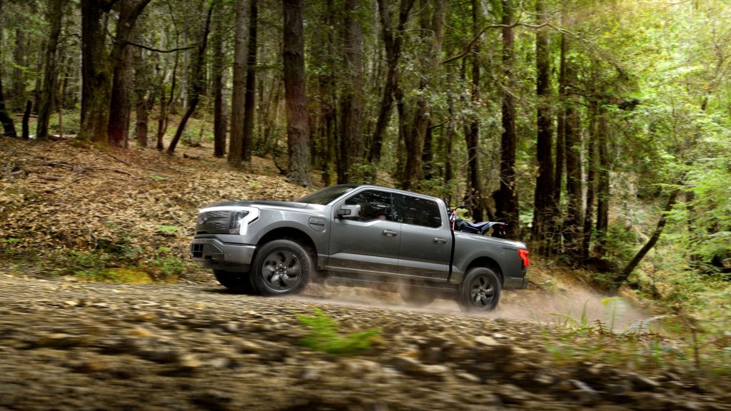 A grey 2022 Ford F-150 Lightning driving on a dirt road in a wooded area.