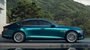 A blue 2022 Genesis Electrified G80 parked next to a tree-covered hill.