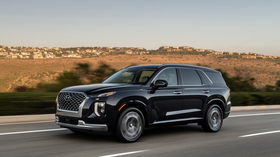 A black 2022 Hyundai Palisade travels on a highway past arid rolling hills on a sunny day