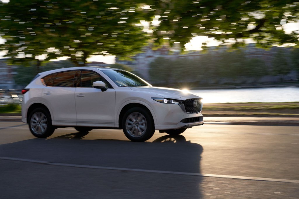 A white 2022 Mazda CX-5 2.5 Turbo Signature compact SUV travels on a road as the sun glints off the hood