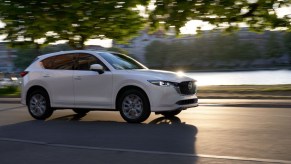 A white 2022 Mazda CX-5 2.5 Turbo Signature compact SUV travels on a road as the sun glints off the hood