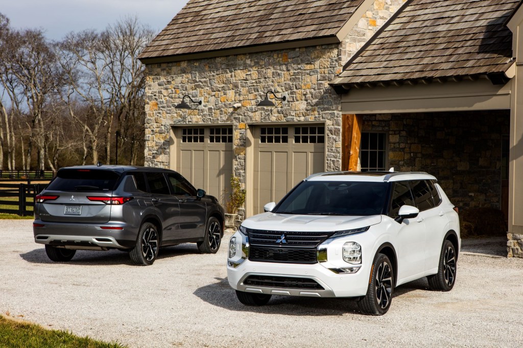 A white and black Mitsubishi Outlander sitting in front of a stone garage.