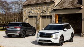 A white and black Mitsubishi Outlander sitting in front of a stone garage.