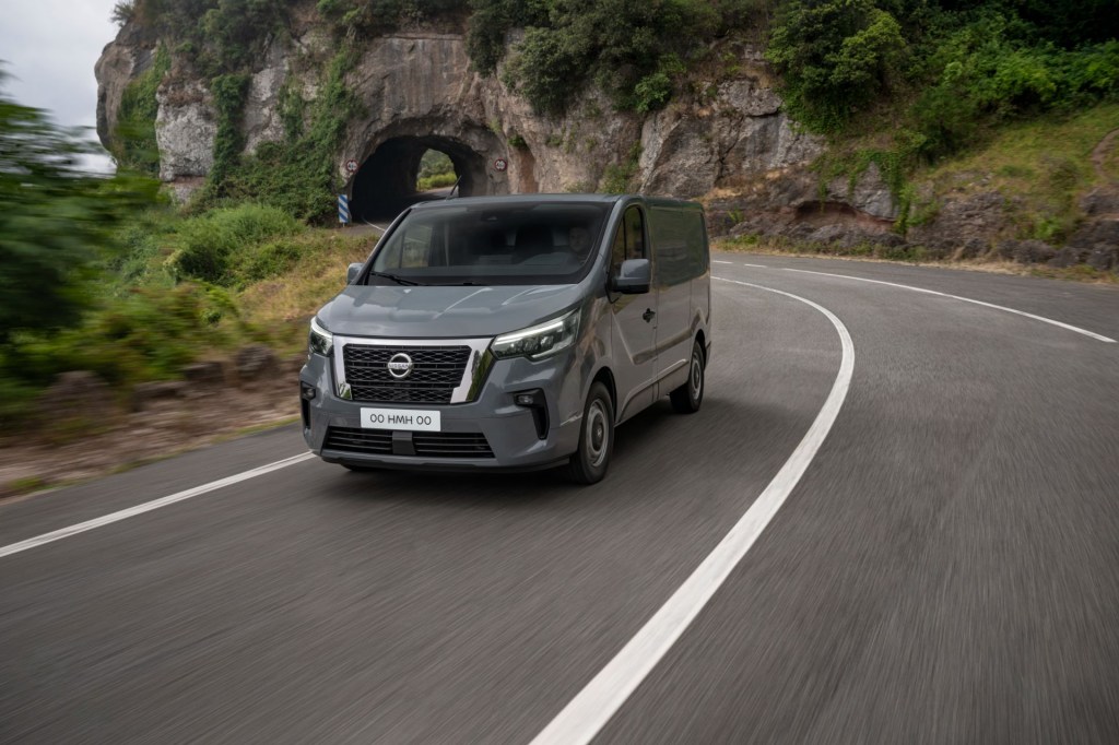 A gray 2022 Nissan Primastar drives down a road near a mountain